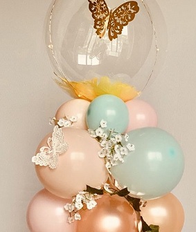 Clear Bubble balloons with yellow petals inside and butterfly sitting on a Cluster of 15 Pink Blue balloons decorated with white flowers