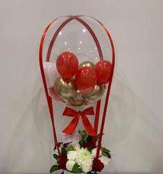 Transparent Balloon stuffed with 3 gold and 3 red balloons Tied with ribbons to a basket of 12 red and white flowers