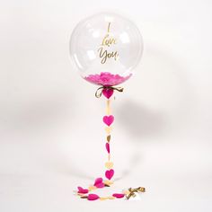 Single Clear blown balloon with pink petals inside and Printed I Love You in gold with trailing 4 hearts on the stem of the balloon