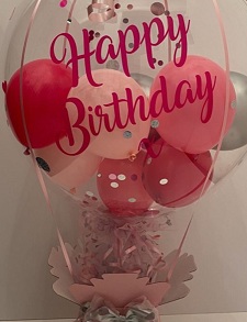 Happy birthday print on balloon with pink and red balloons inside the clear balloon tied to a box with pink and red paper wrapping